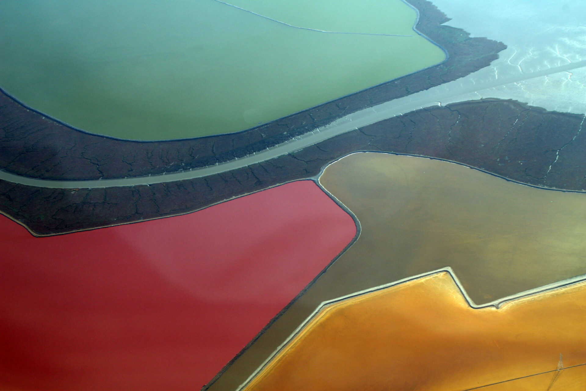 A slough bordered by marsh cutting through colorful bright red, green, and yellow = salt evaporation ponds